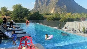 Ein Swimmingpool mit Holzliegen, ein Kind in einem pinkfarbenen Schwimmreifen und ein Berg im Hintergrund.