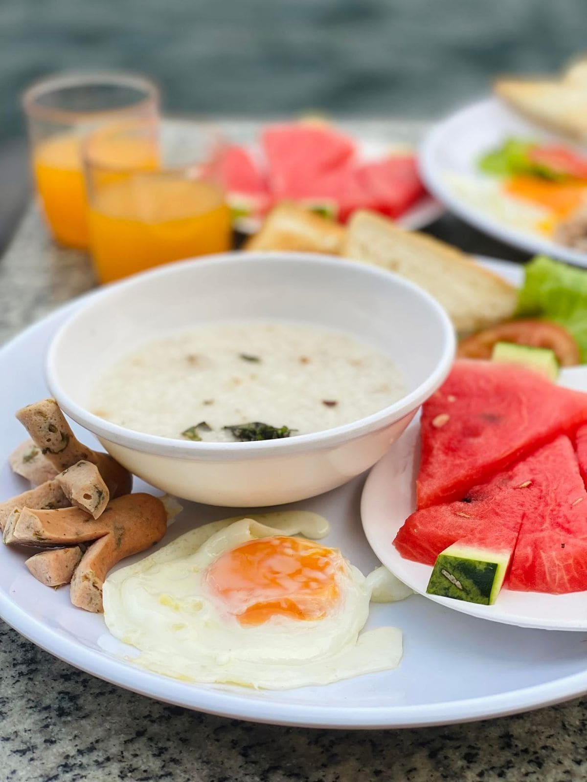 A breakfast plate with scrambled eggs, sausage, and watermelon slices.