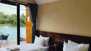 Ein Hotelzimmer mit zwei Betten, einem Holz-Kopfstück und Blick auf ein Gewässer durch große Fenster.