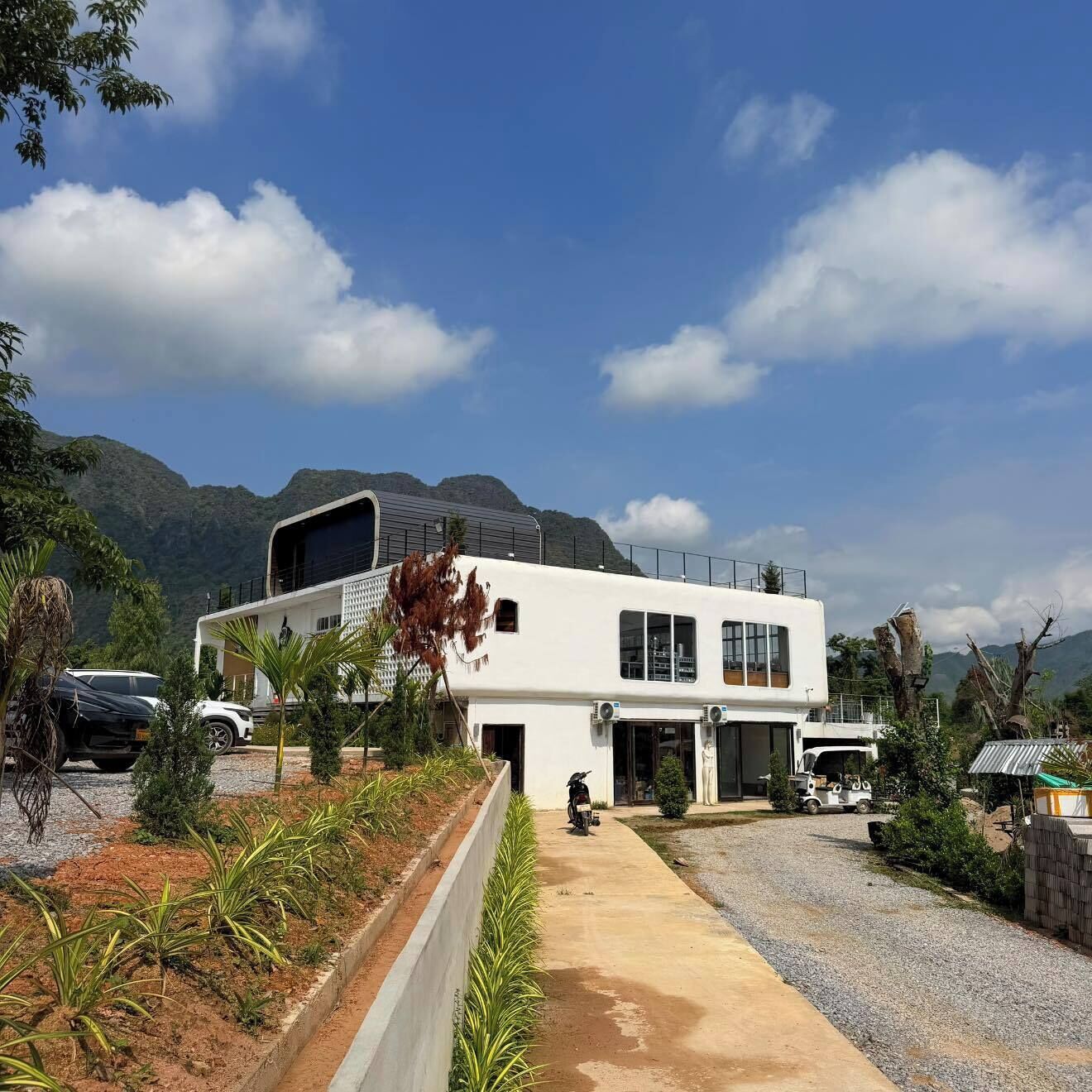 A modern building with a flat roof, large windows, and a gravel driveway.