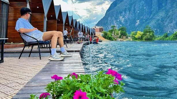 Eine Holzterrasse mit einer Person beim Angeln, mit Blick auf ein Gewässer und Berge.