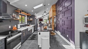 A modern kitchen with a central island, built-in appliances, and a unique purple accent wall. - Dream Escape l Near Kalahari Camelback&Casino l Game Room l Fire Pit l Projector (Tobyhanna)