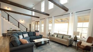 A spacious living room with a staircase, two sofas, a coffee table, and large windows. - Game & Movie Room, Minutes to Wine, Weddings &Town (Lumpkin County)