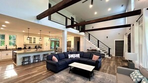 A spacious living area with a dark-colored sectional sofa, a coffee table, and a staircase leading to an upper level. - Game & Movie Room, Minutes to Wine, Weddings &Town (Lumpkin County)