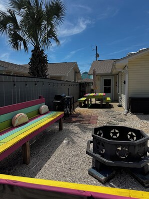A backyard with a colorful bench, a grill, and a fire pit. - Charming 2-bedroom house in gorgeous PCB just steps away from the beach (Panama City Beach)