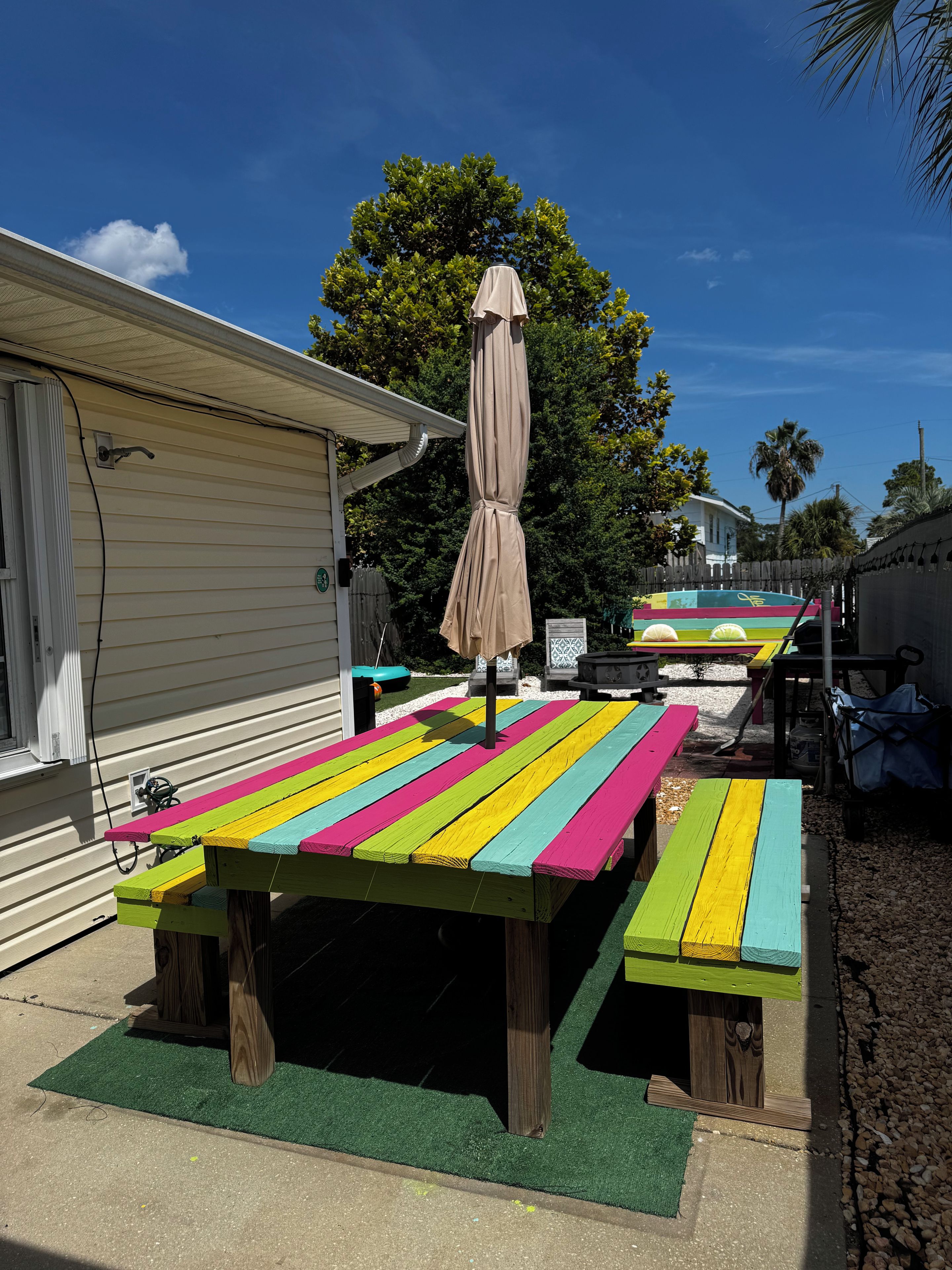 A colorful picnic table with a canopy, set against a backdrop of a house and trees.