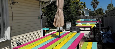 Una mesa de picnic colorida con toldo, frente a una casa y árboles.