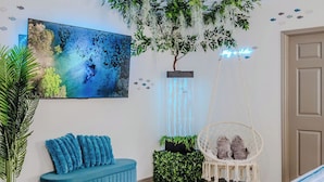 A room with a blue sofa, a hanging plant, a wall-mounted aquarium, and a neon sign.