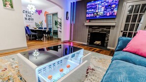 A modern living room with a glass coffee table, a flat-screen TV mounted on the wall, and a blue sofa.