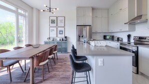 Una cocina moderna con una isla grande, armarios blancos y una zona de comedor con mesa y sillas de madera.