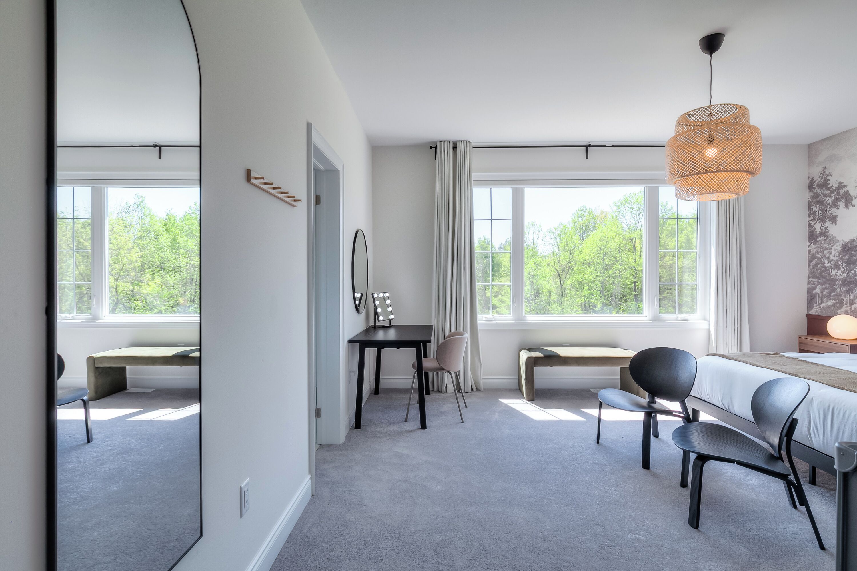 Une chambre d’hôtel moderne dotée d’une grande fenêtre, d’un bureau avec une chaise, d’un banc et d’un lit avec une tête de lit.