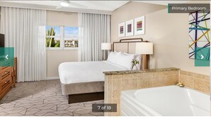 Un dormitorio principal con cama, tocador con bañera, ventana con cortinas y vista a edificios.