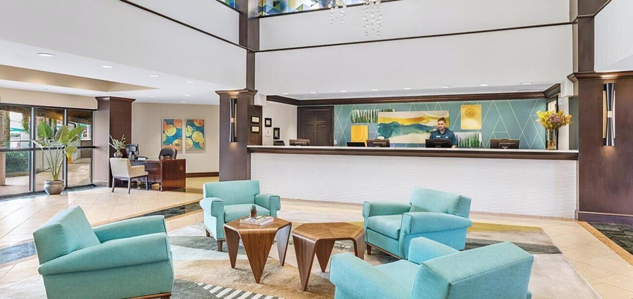 Um lobby com poltronas azuis-esverdeadas, um balcão de recepção e uma janela grande.