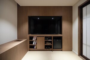 A modern living room with a built-in TV, wooden shelving, and a compact refrigerator.