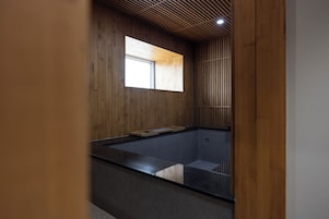 Un baño moderno con pared de madera, una ventana pequeña y una bañera de vidrio.
