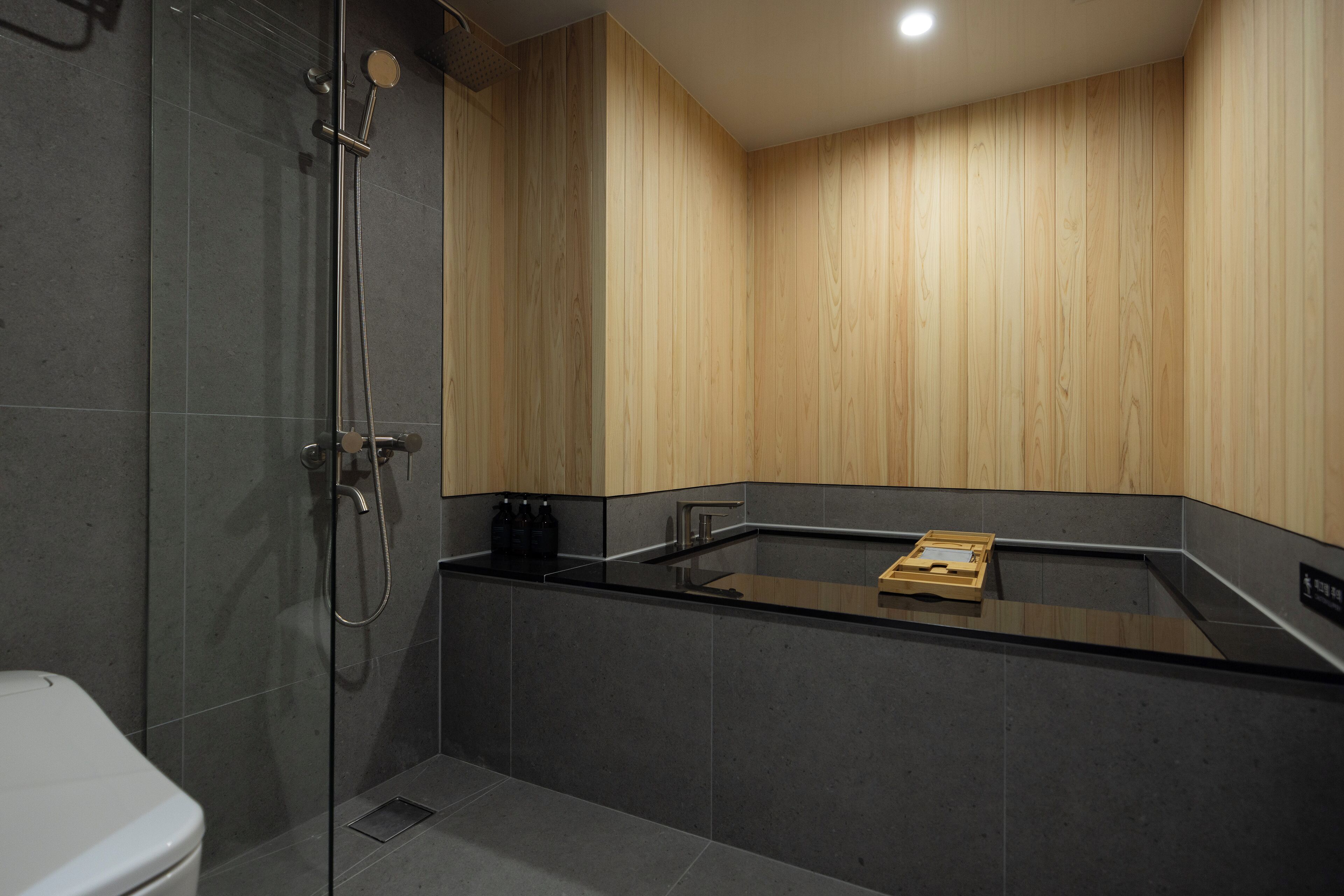 A modern bathroom with a glass-enclosed shower, a black countertop, and wooden panel walls.