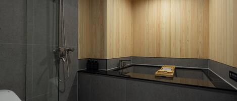 A modern bathroom with a glass-enclosed shower, a black countertop, and wooden panel walls.