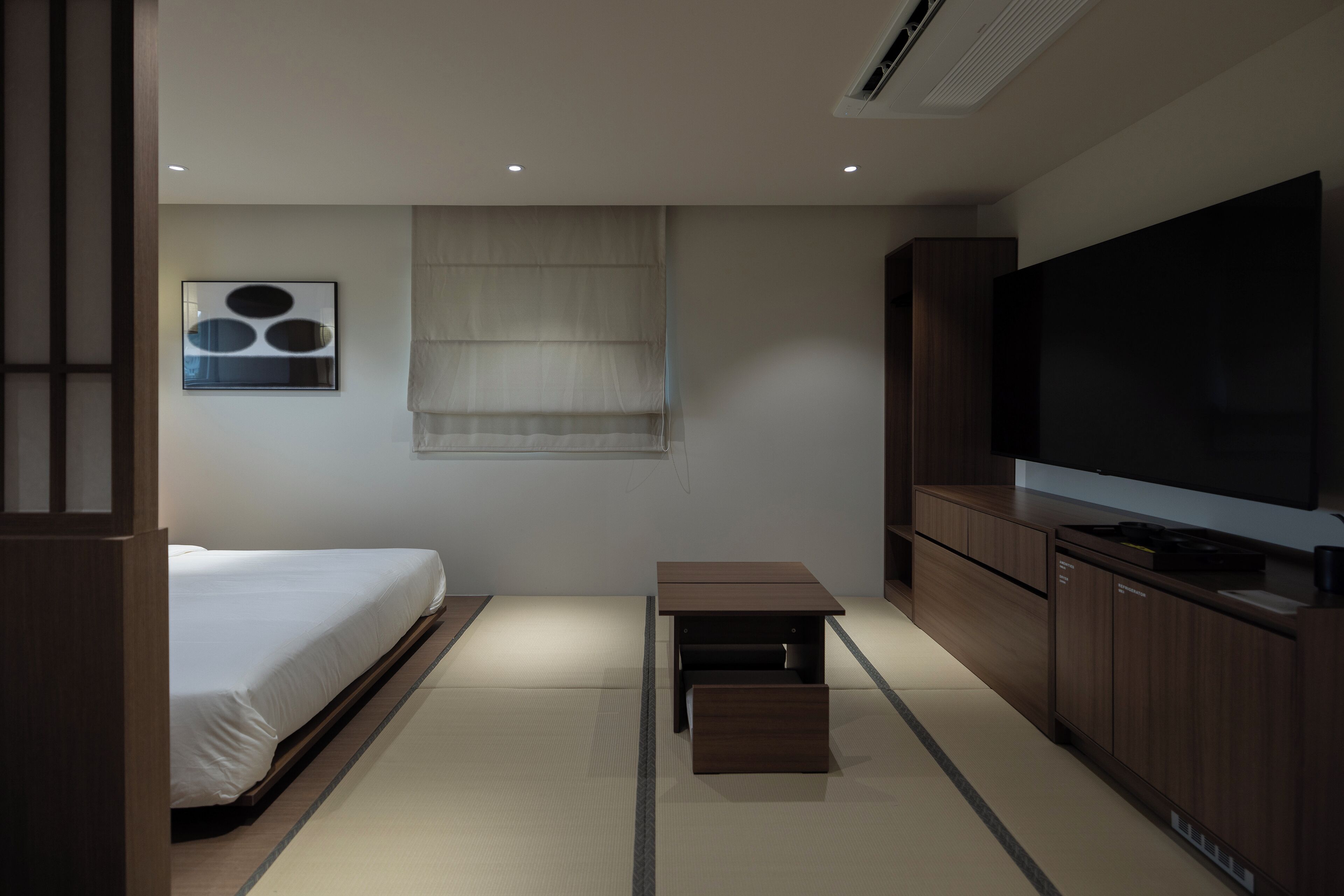 A modern hotel room with a bed, a small table, a TV, and a cabinet.