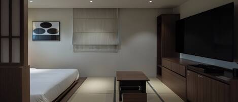 A modern hotel room with a bed, a small table, a TV, and a cabinet.