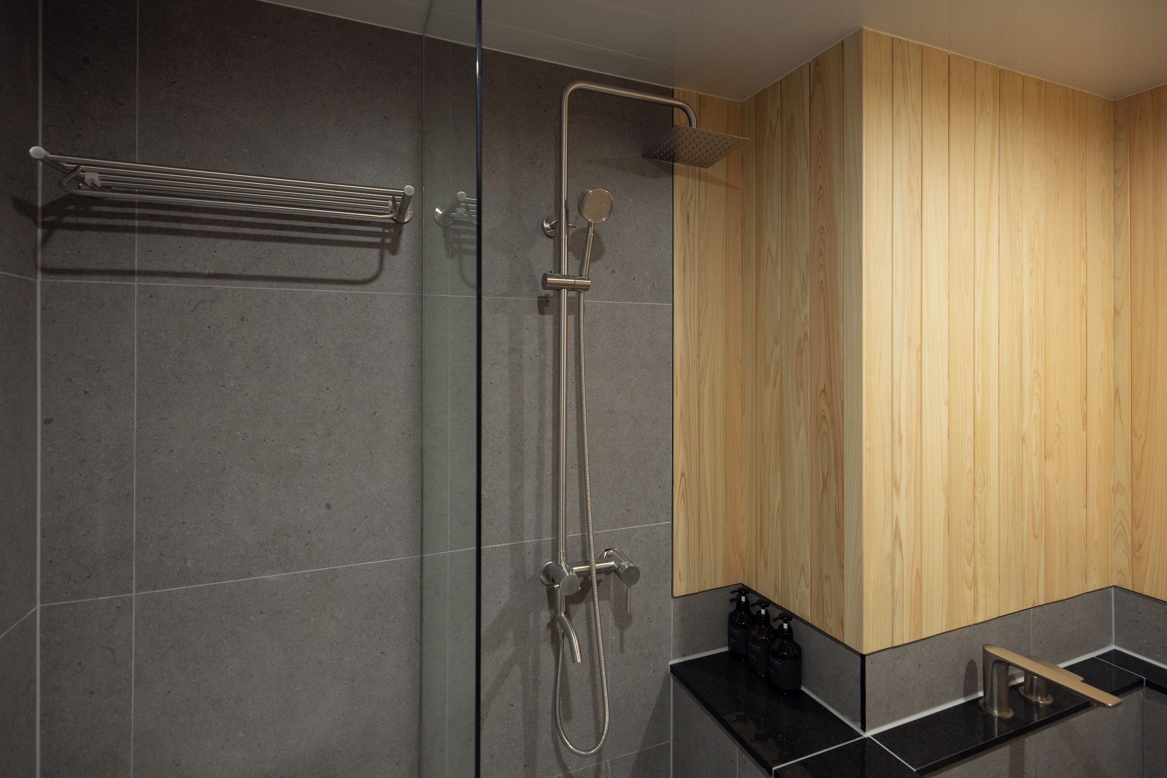 A modern bathroom with a glass shower enclosure, a wooden wall panel, and a black countertop.