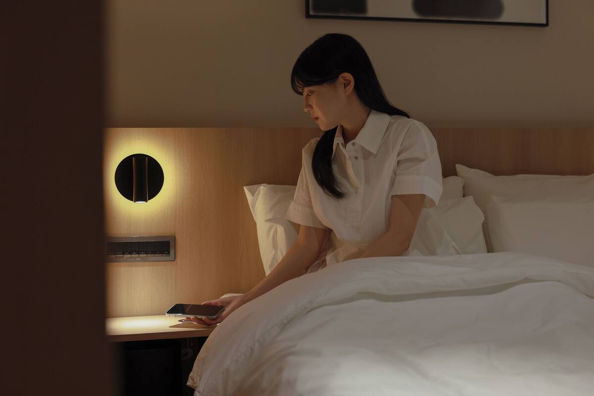 A hotel room with a bed, a bedside table, and a wall-mounted light fixture.