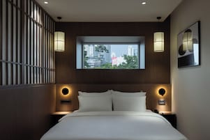 Habitación de hotel con una cama grande, dos mesitas de noche, un ventanal con vistas a la ciudad e iluminación en la pared.
