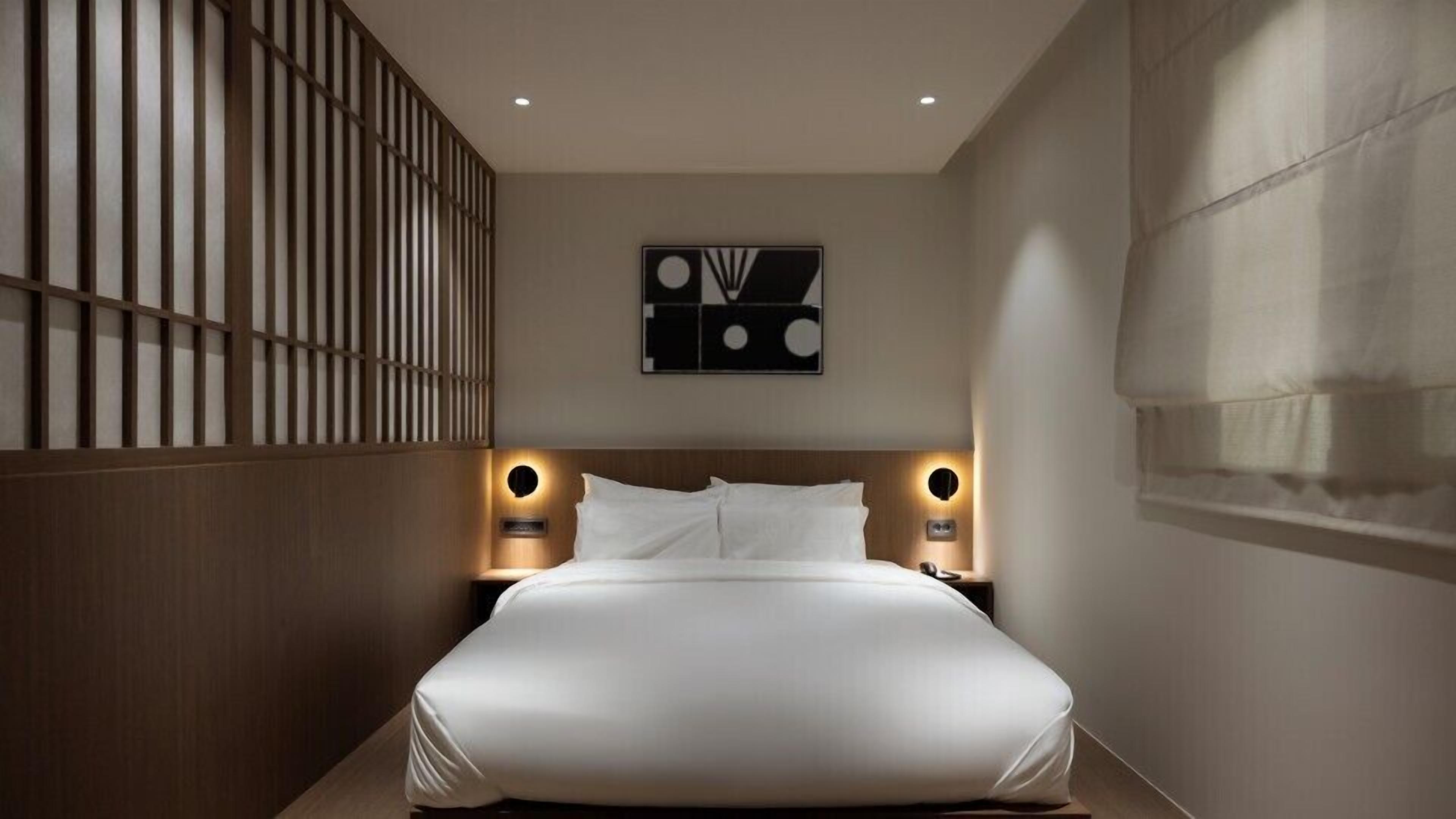 Una habitación de hotel moderna con una cama grande, paneles de madera en una pared y una obra de arte abstracta colgada en la pared.