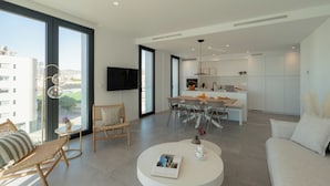 Una sala moderna con una mesita redonda, un sofá y un comedor con sillas, y una cocina al fondo.