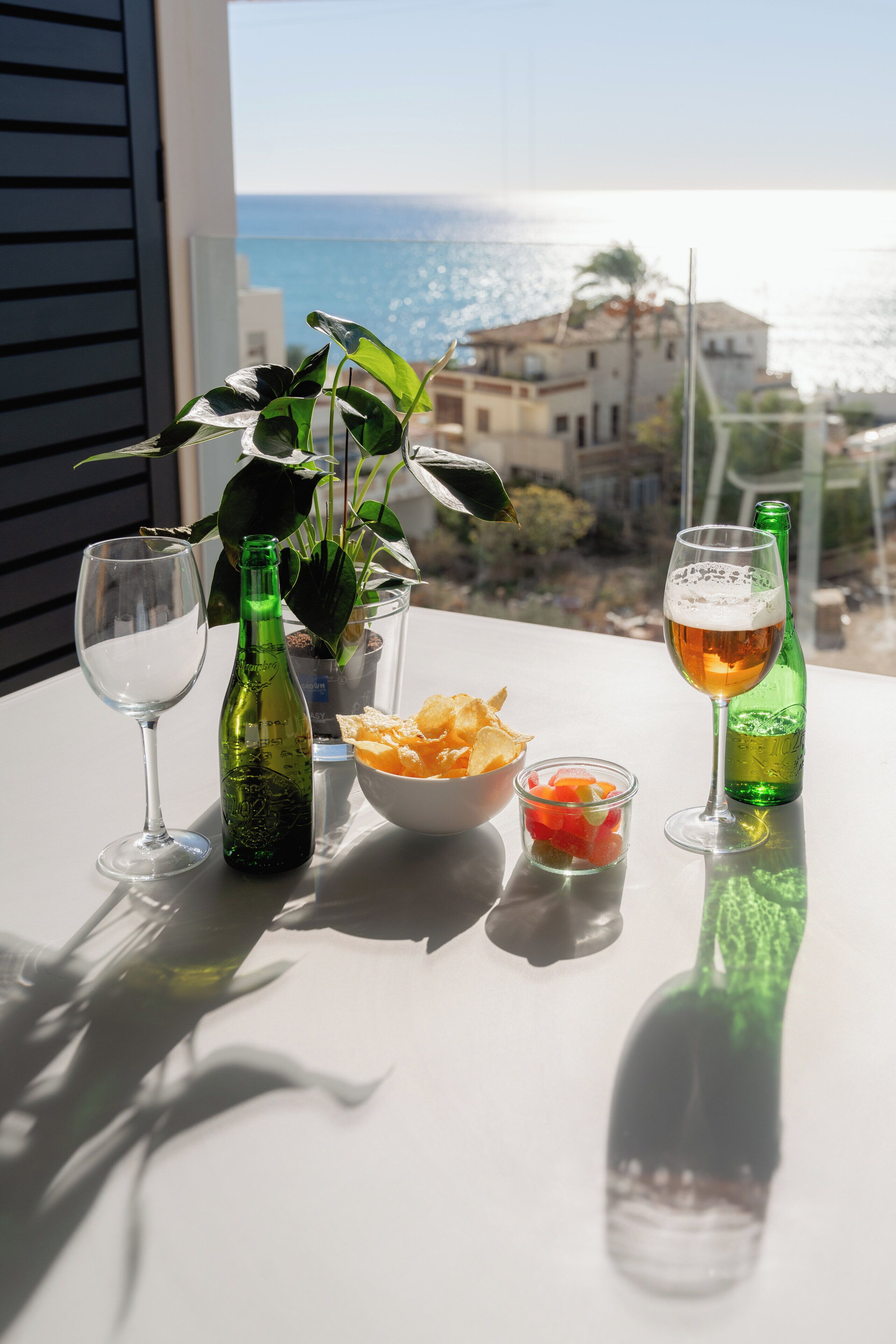 Una mesa con una botella verde, una cerveza, un tazón de papas fritas y un vaso de agua.