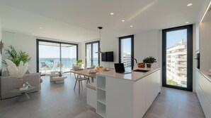 Una cocina moderna con una isla central, comedor con sillas y ventanas amplias con vista al mar.