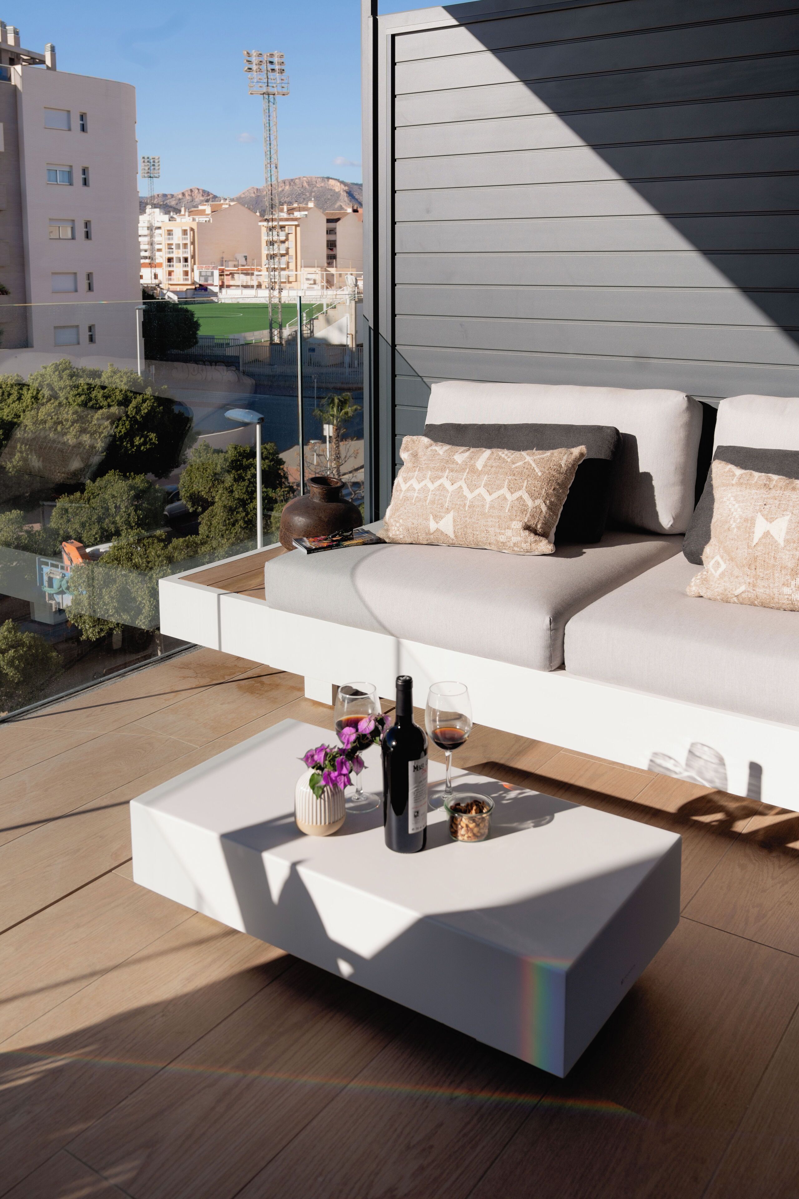 Un área de estar moderna al aire libre con un sofá, una mesa de centro, una botella de vino y un florero con flores.