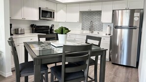 Une cuisine moderne avec des meubles blancs, un réfrigérateur en acier inoxydable, un four à micro-ondes et une table à manger avec des chaises.