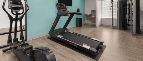 Ein Fitnessraum mit Cardiogeräten, einem an der Wand montierten Fernseher und einer Trinkstation.
