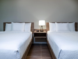 A hotel room with two beds, a nightstand with a lamp, and a wooden floor.