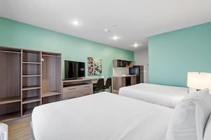 Quarto de hotel com duas camas, uma escrivaninha, televisão, micro-ondas e guarda-roupa.