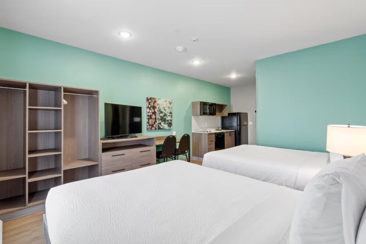 Une chambre d’hôtel avec deux lits, un bureau avec une chaise, une télévision, un four à micro-ondes et une armoire.