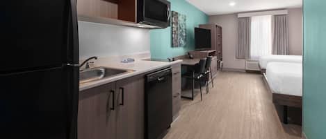 A compact hotel room with a kitchenette, a bed, a desk, and a television.