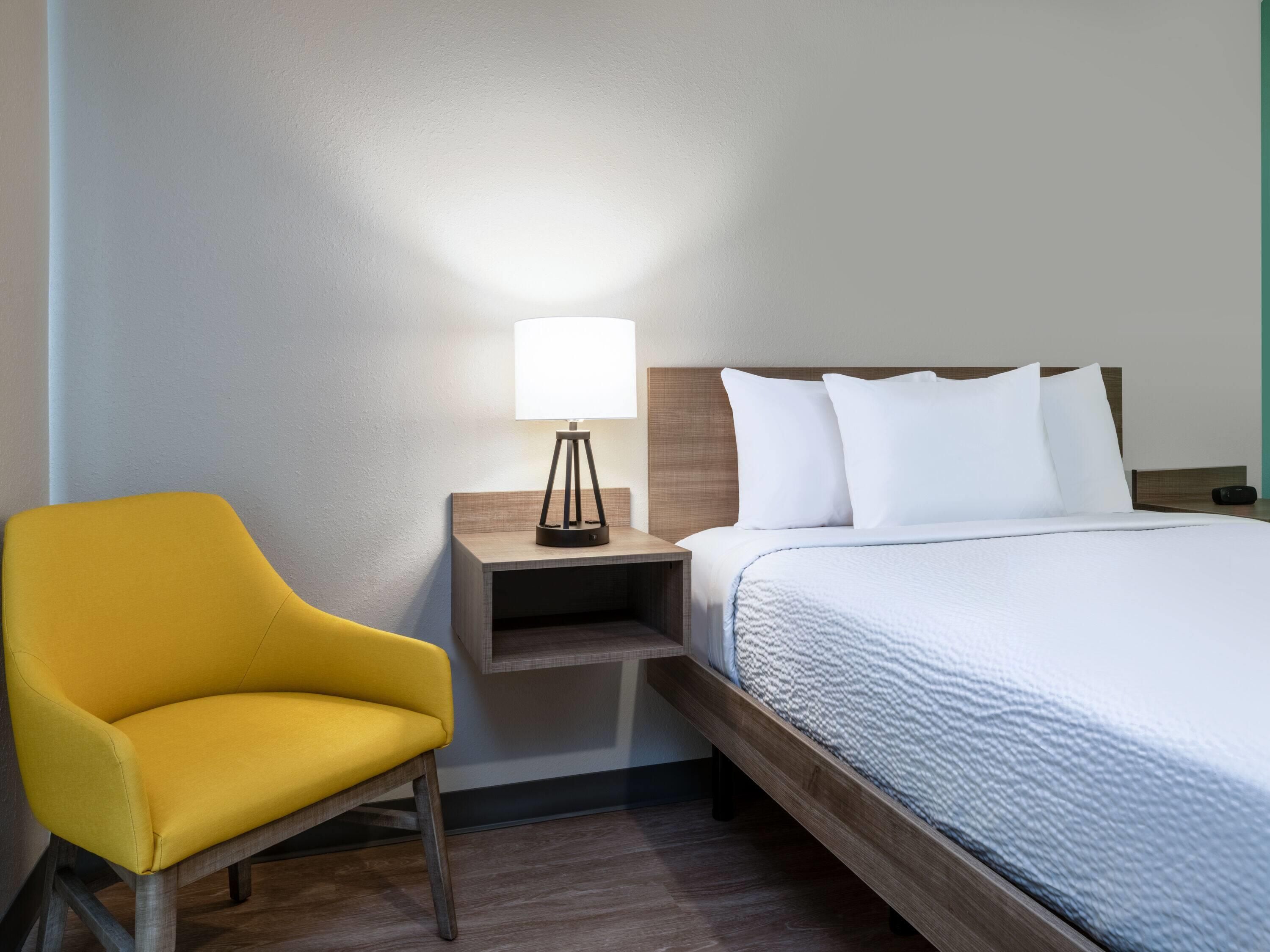 A hotel room with a bed, a nightstand, a lamp, and a yellow chair.