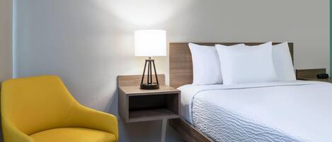Habitación de hotel con una cama, una mesita de noche, una lámpara y una silla amarilla.