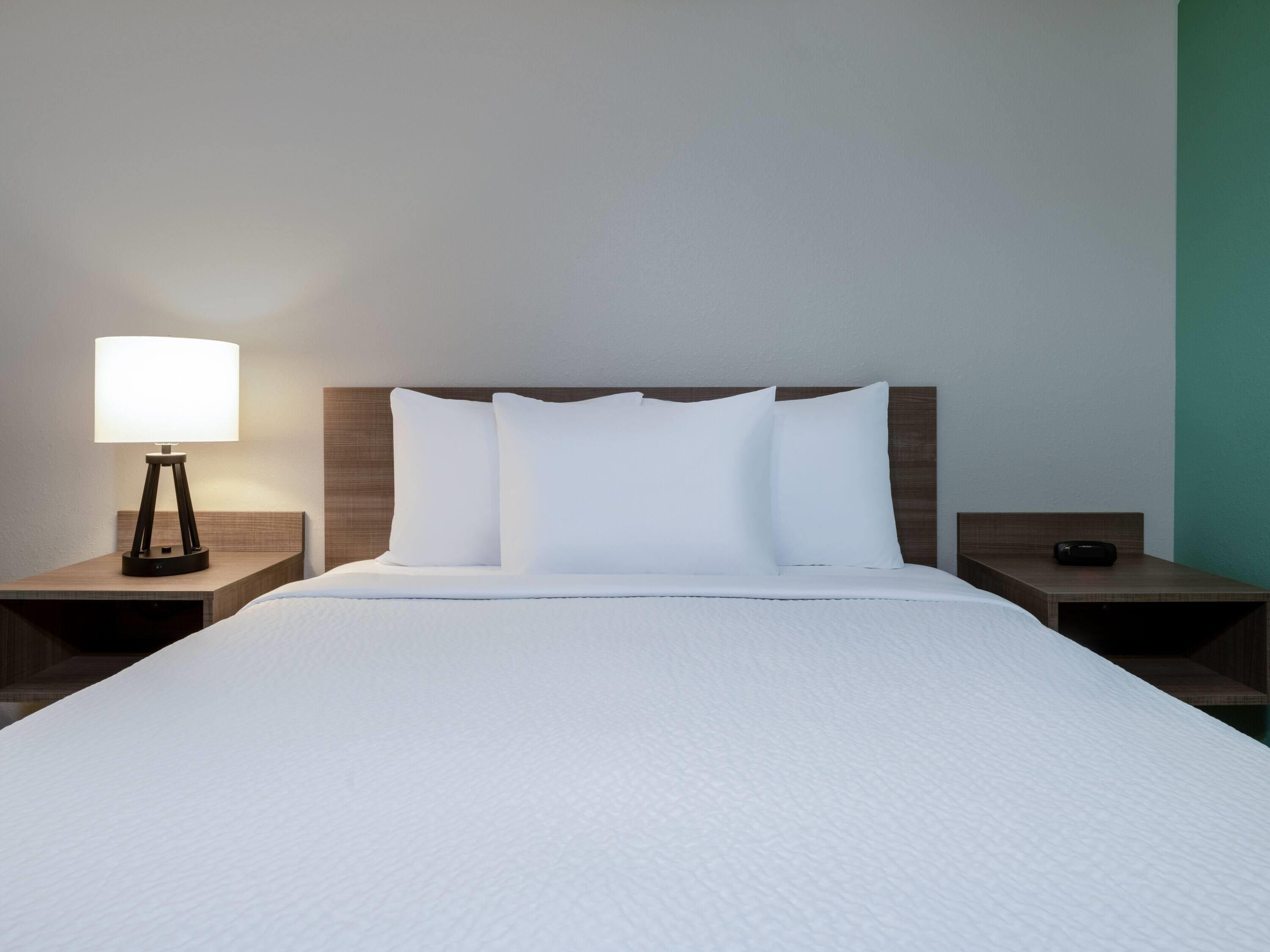 A neatly made bed with white linens, a bedside lamp, and a nightstand with a remote control.