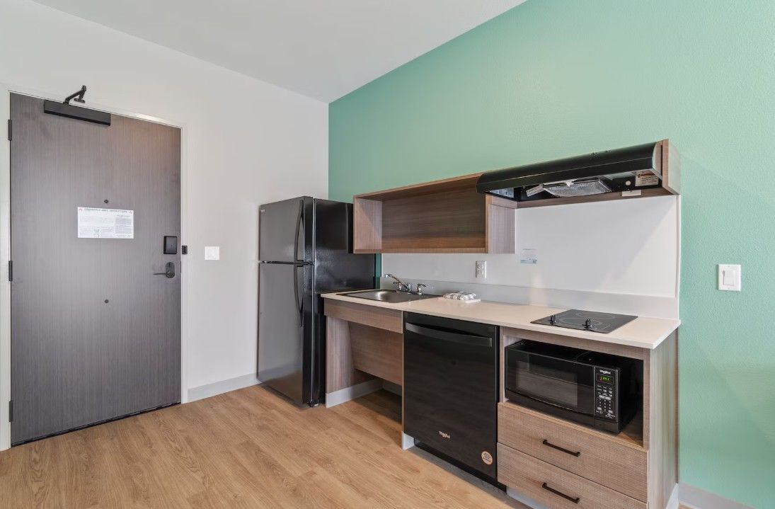 A compact kitchen with a refrigerator, microwave, dishwasher, and wooden cabinets.