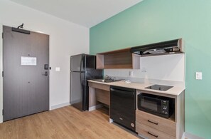 Une cuisine compacte équipée d’un réfrigérateur, d’un four à micro-ondes, d’un lave-vaisselle et de meubles de rangement en bois.