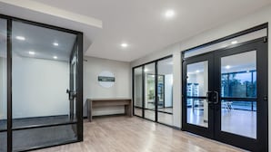A modern hotel lobby with glass doors, a reception desk, and a view of the outdoors.