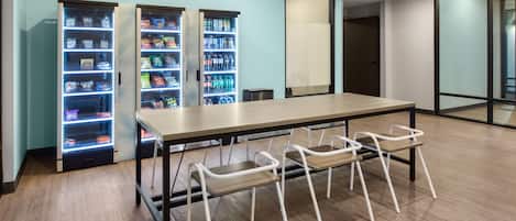 Une pièce moderne avec une longue table, quatre chaises blanches et deux distributeurs automatiques.
