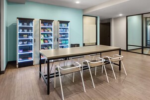 A modern room with a long table, four white chairs, and two vending machines.