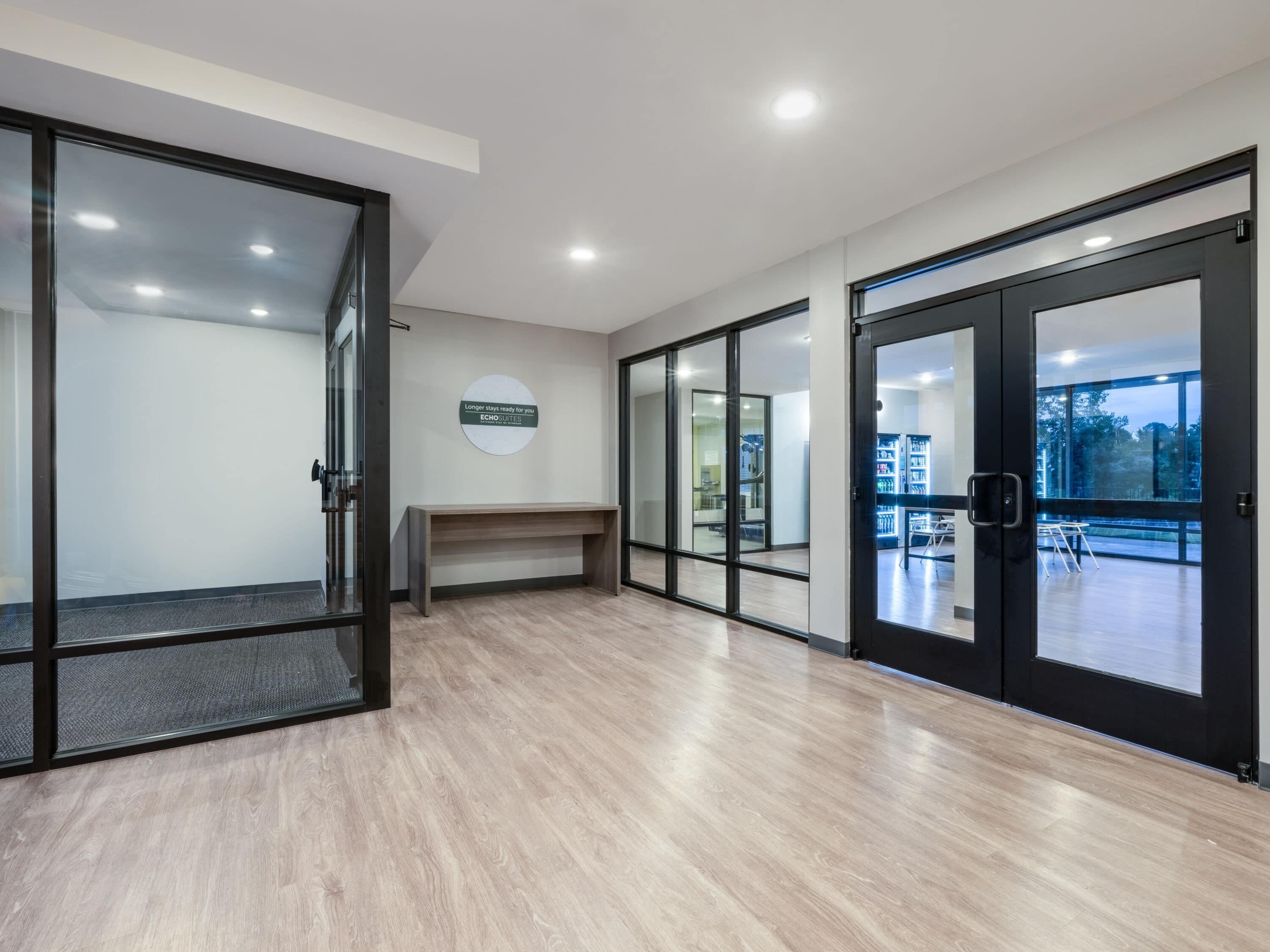 A modern hotel lobby with glass doors, a reception desk, and a view of the outdoors.