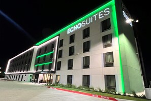 A hotel named ECHOSUITES with a modern facade, illuminated green accents, and a fire lane in front. - Echo Suites Extended Stay Wyndham Ft Worth Allianc (Keller)