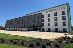 A modern hotel building with the name 'Echosuites' on the facade. It features a flat roof, multiple windows, and a parking lot in front.