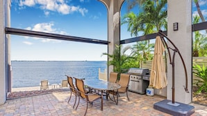 An outdoor patio with a table and chairs, a grill, and a view of the water. - VRCC Villa Dolphin House (Cape Coral)