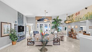 A spacious living area with a glass coffee table, a large potted plant, and a ceiling fan. - VRCC Villa Dolphin House (Cape Coral)
